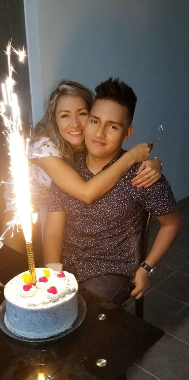 Olga abraza a su hijo Juan Camilo, sonriendo, frente a un pastel de cumpleaños con una vela de chispas